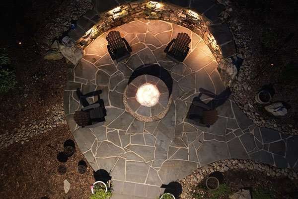 laughter family hardscapes image 3 Outdoor hardscaping design featuring a circular stone fire pit surrounded by wooden chairs, illuminated at night, showcasing Laughter Family Hardscapes' custom landscaping work in Asheville, NC.