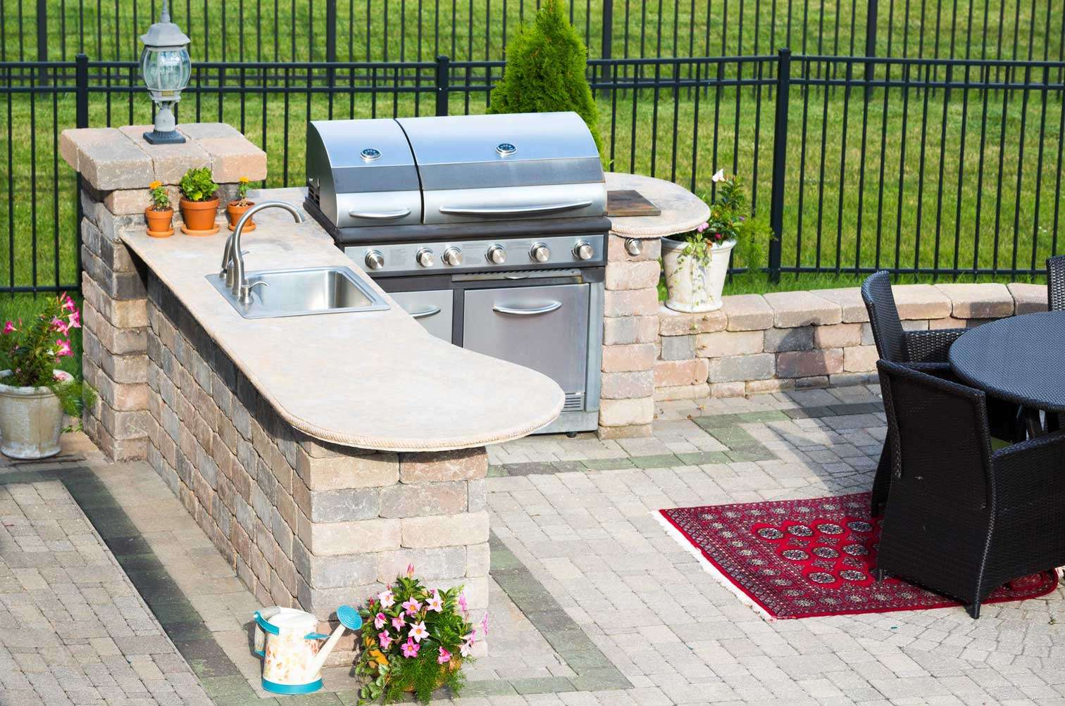 Masonry outdoor kitchen with a built-in grill, sink, rounded counters, and a paver patio