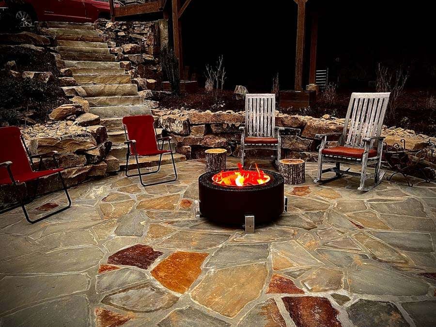 Laughter Family Hardscapes Hardscaping Services Buncombe County NC -03 Fire pit surrounded by stone patio, red and white chairs, and rustic wooden stools in a cozy outdoor setting, showcasing hardscaping features for enhancing outdoor living spaces in Etowah, NC.