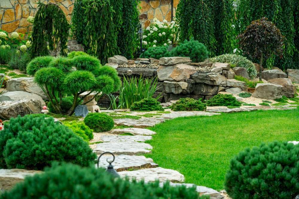 A beautifully landscaped garden in Etowah, NC, featuring lush greenery, stone pathways, and a serene rock water feature, showcasing expert landscaping services.
