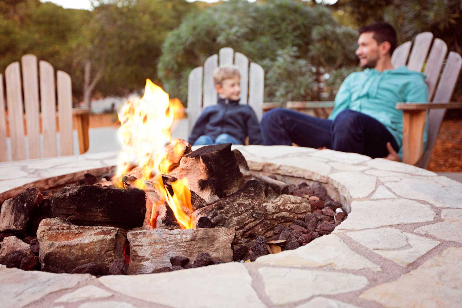 Natural-stone fire pit with a broad flagstone surround in a backyard seating area