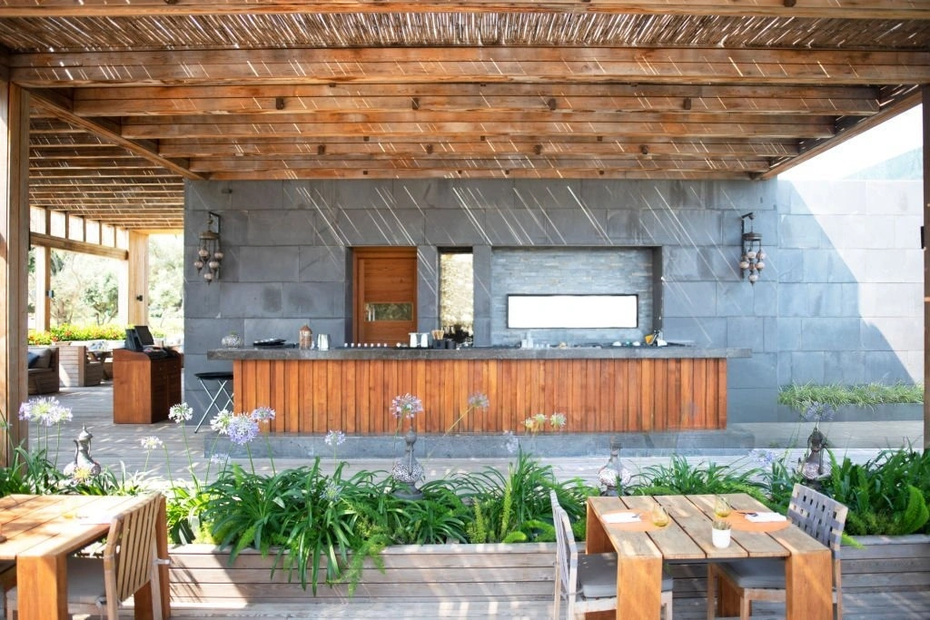 outdoor kitchen Custom outdoor kitchen with stone island, wooden accents, and bar-style seating, surrounded by lush greenery and patio dining area, enhancing outdoor entertaining space.