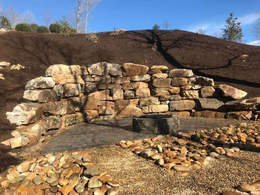 Large natural stone retaining wall holding a cut soil slope