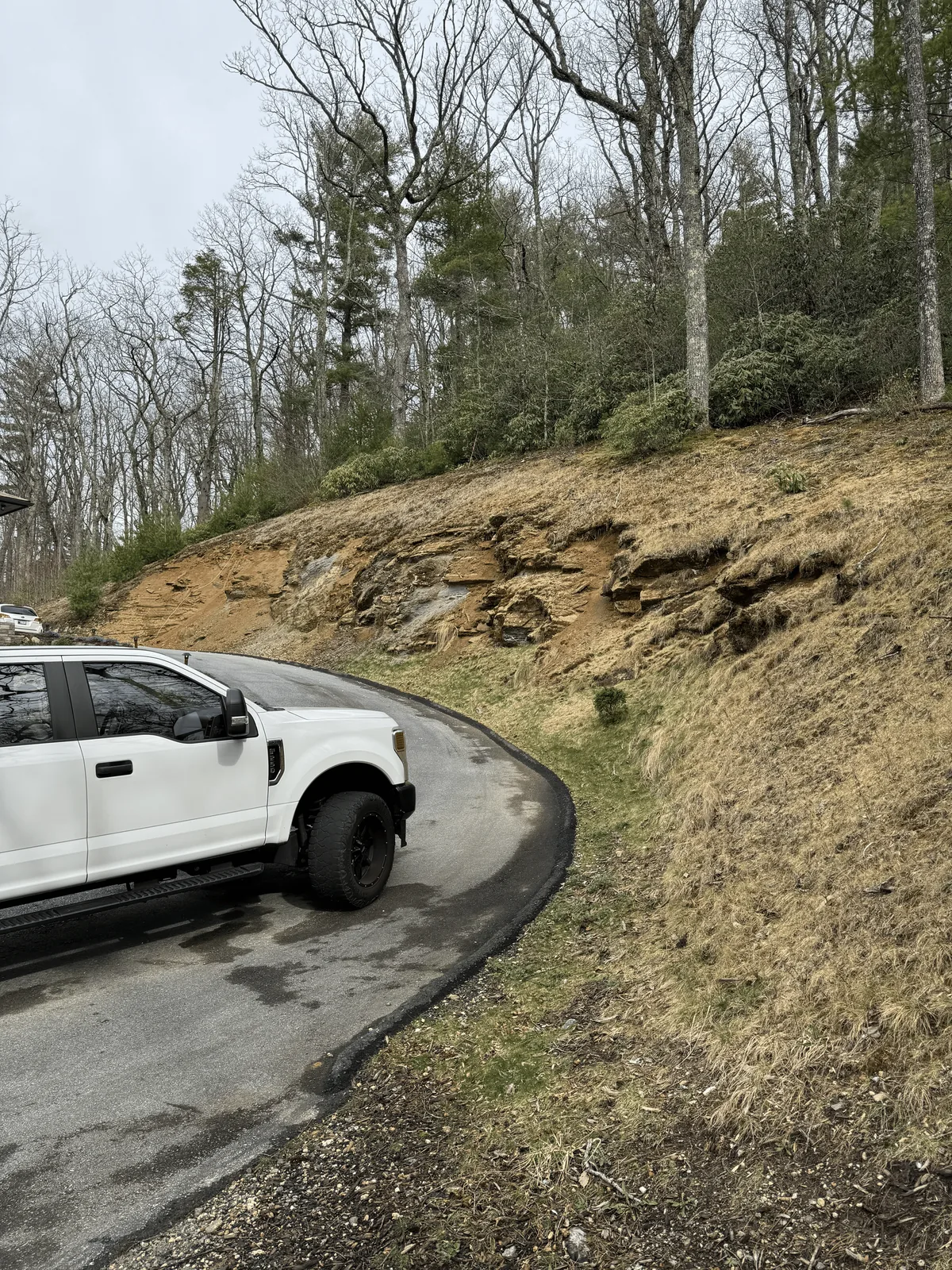 Steep exposed slope beside a residential driveway before retaining wall construction