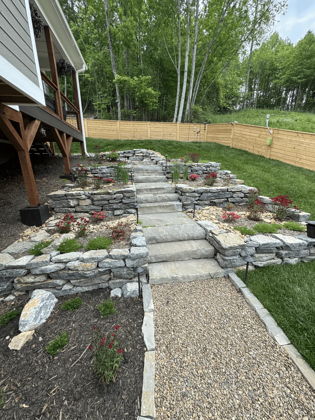 Tiered stone retaining walls and steps creating access across a sloped yard
